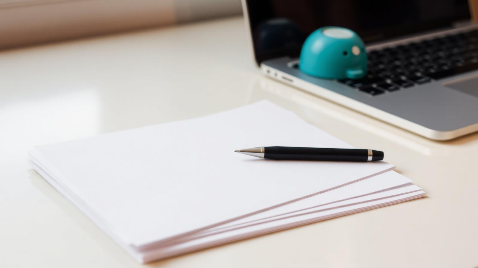 Een stapel geordende facturen op een licht bureau, met een pen en een laptop ernaast.